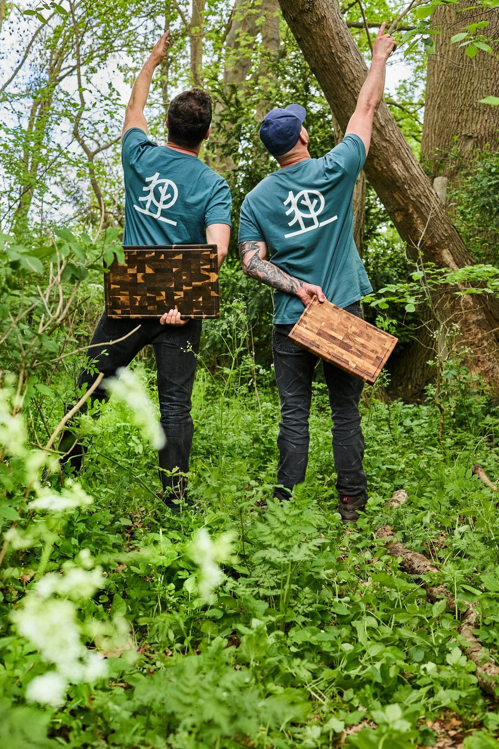 Foto: Falko und Christoph von hinten im Wald, in grünen Klingenholz-Shirts, jeder mit einem Brett in der Hand.